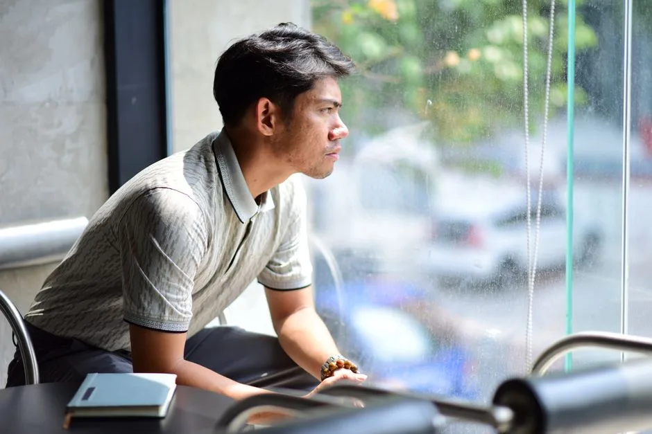 A man sitting alone by a window, deep in thought