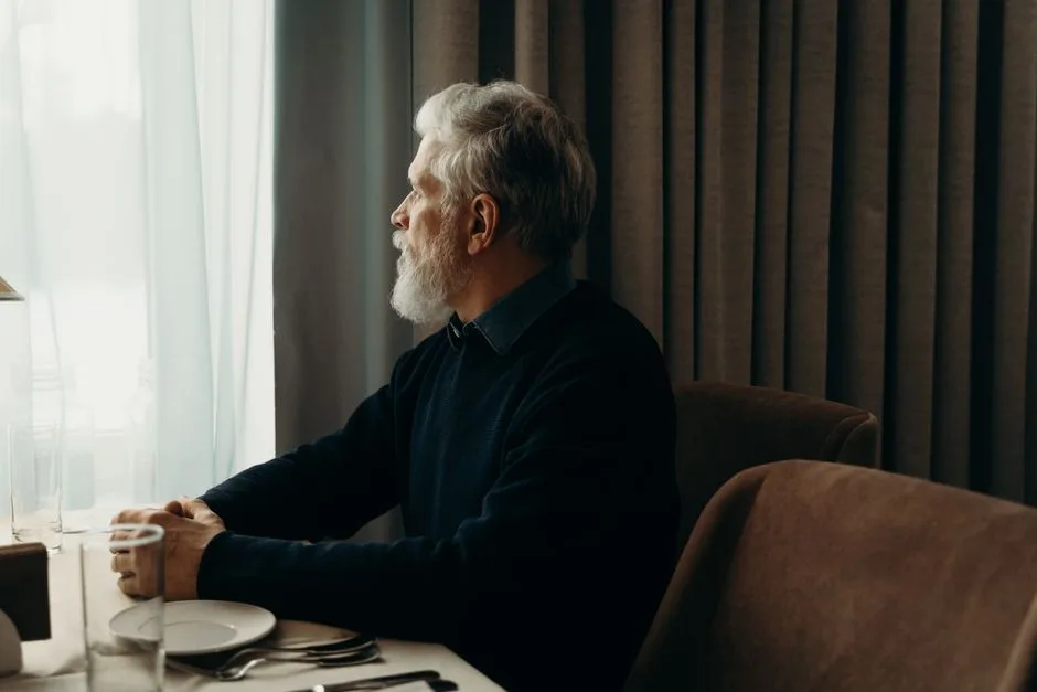 A retired man sitting quietly by a window, deep in thought