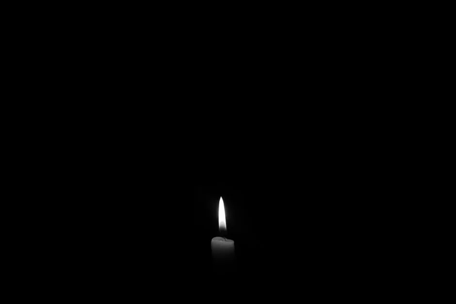 A single candle flame in darkness — light that holds even in the presence of death