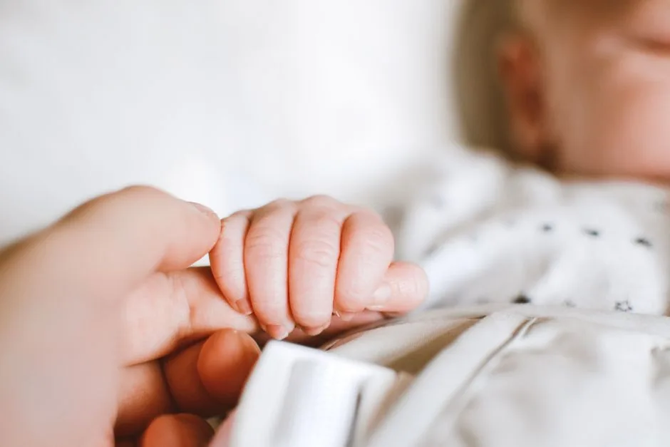 A newborn's hand grasping a parent's finger — the deliberate, careful craftsmanship behind every human life