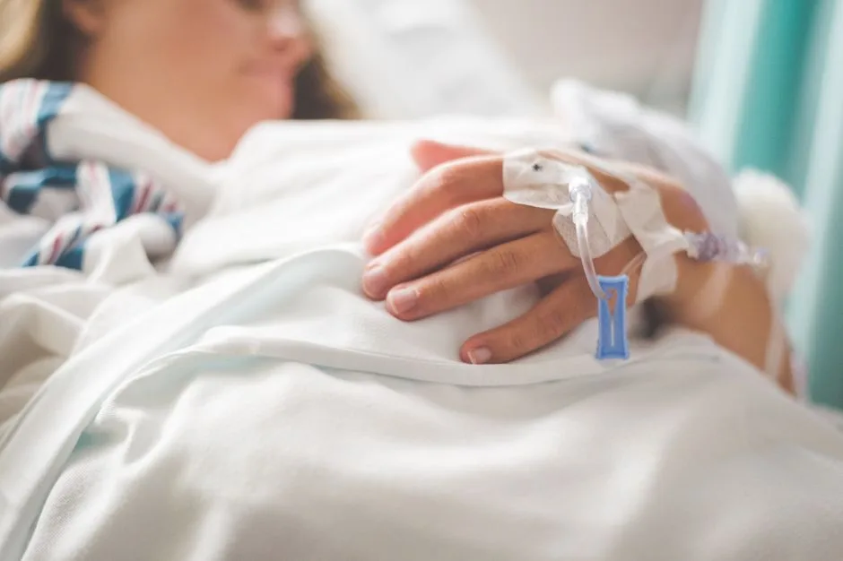 Hands gently resting on a hospital bed rail — illness held without the weight of unwarranted guilt