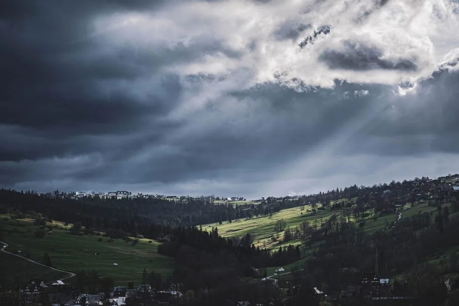 Sunlight breaking through clouds in three distinct rays converging — the unity and distinction within the Trinity