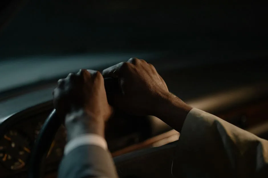 A worker's hands gripping a steering wheel at dawn — ordinary work offered with genuine purpose